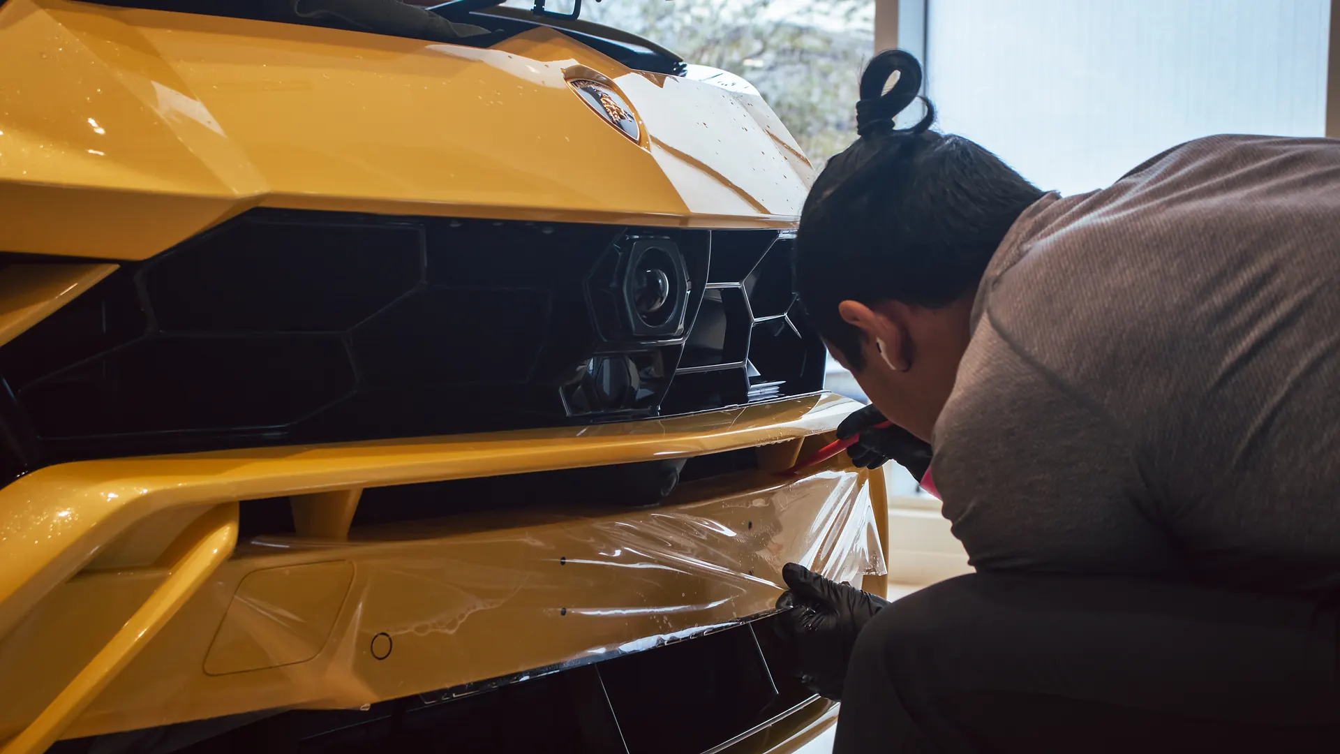Technician applying paint protection film to a yellow Lamborghini Urus front bumper at Elements Labs.