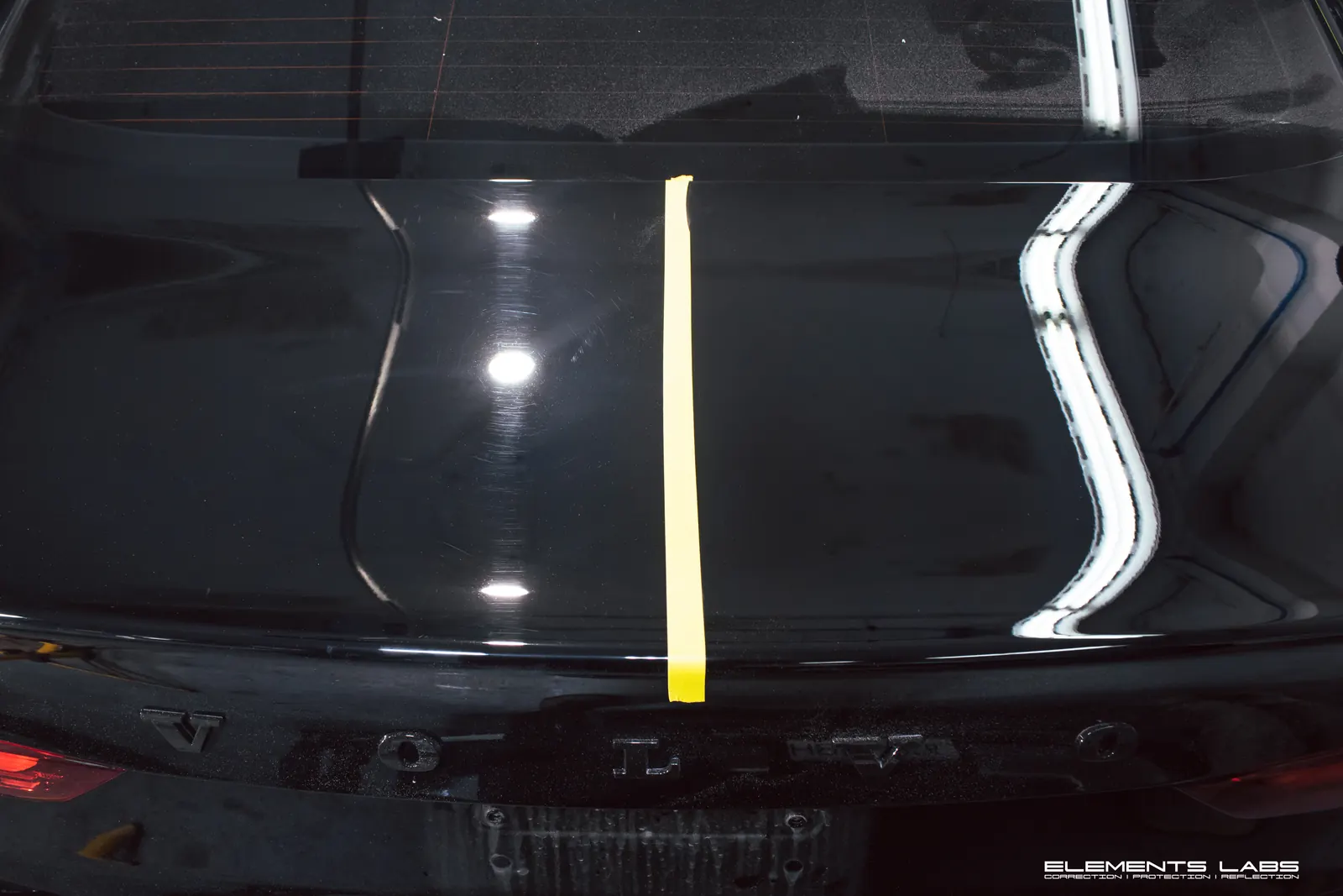 Black Volvo tailgate divided by tape to show paint swirls before correction and improved clarity after correction