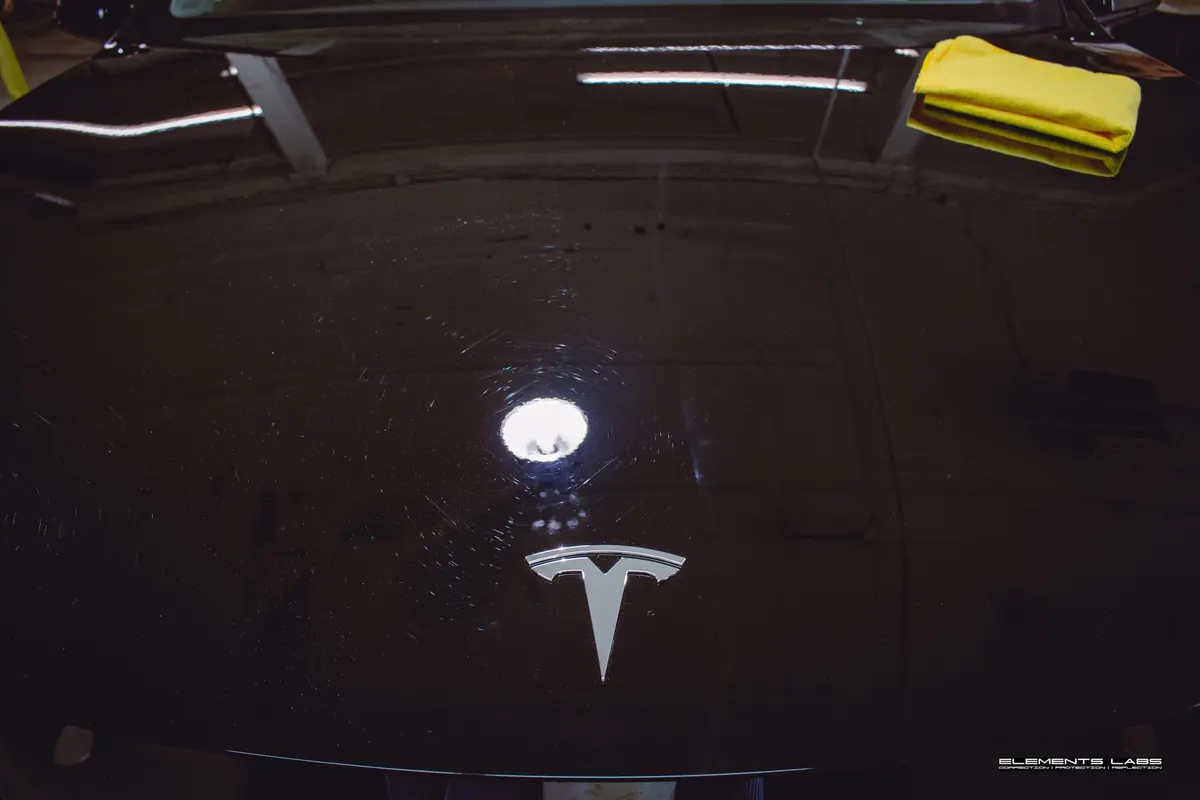 Swirls visible under inspection lighting on a black vehicle hood at Elements Labs