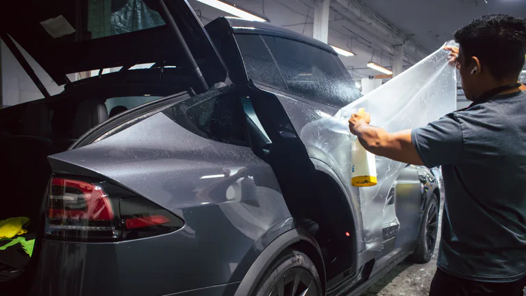 Technician applying clear paint protection film to the side of a grey Tesla Model X.